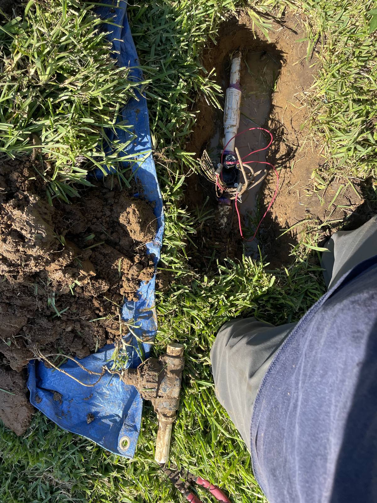 Excavated sprinkler valve in a Hurst, Texas lawn with the replacement valve in the hole, red wiring beside it, and the removed valve lying on the grass