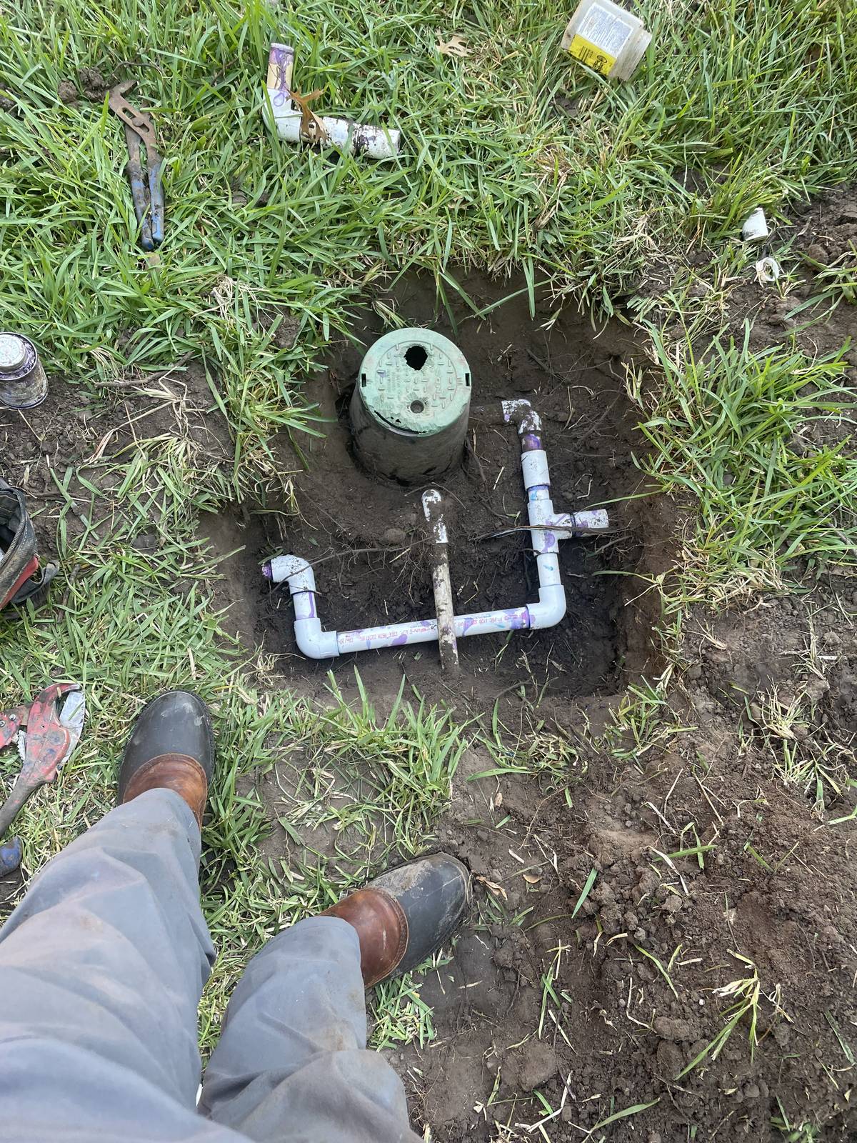 Dug-out irrigation valve location in North Richland Hills, Texas with new PVC fittings installed beside a round green valve box