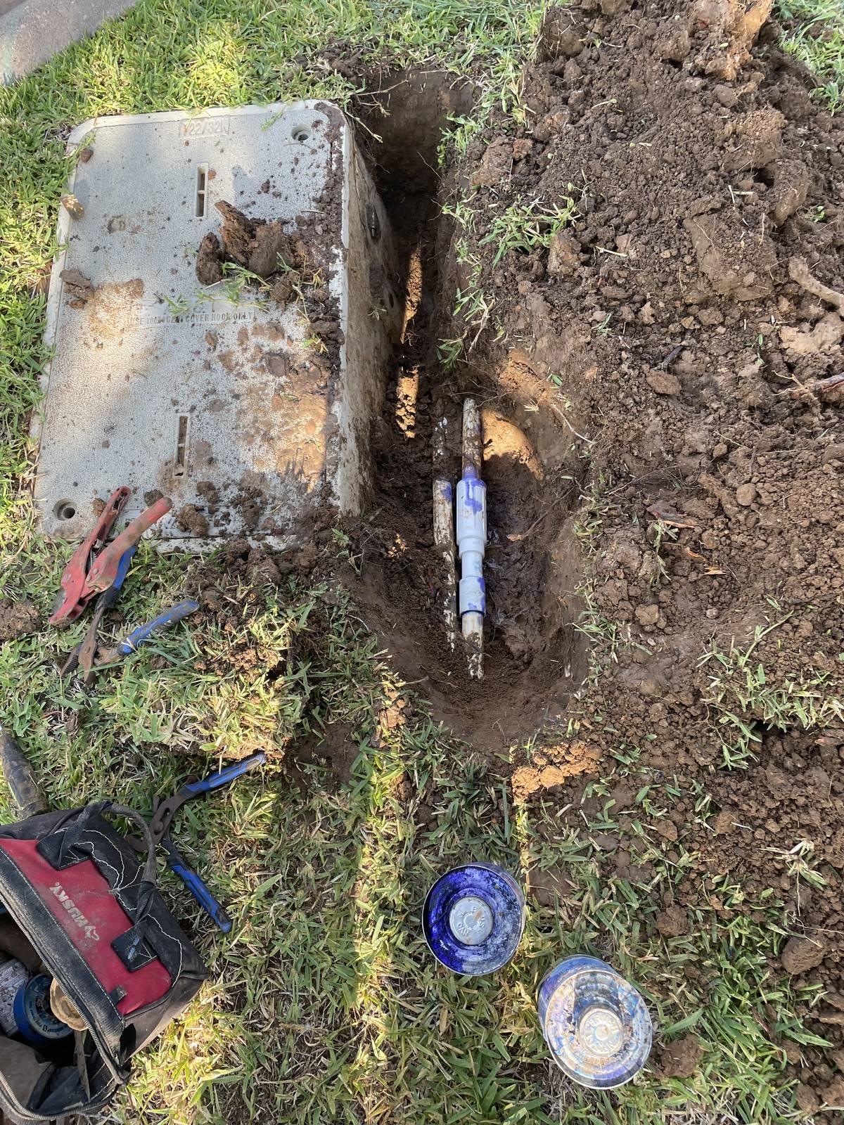 Repaired PVC sprinkler pipe joined with new couplings in a trench in North Richland Hills, Texas, with primer and cement cans beside it